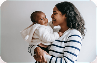 Woman smiling and holding a baby in a white fuzzy jacket.