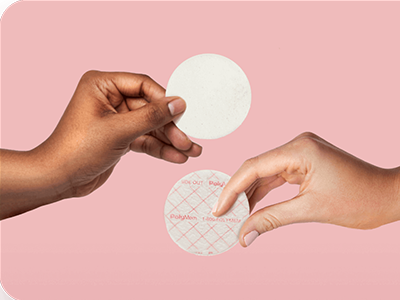 Two hands holding Nursicare Therapeutic Breast Pads over a pink background.